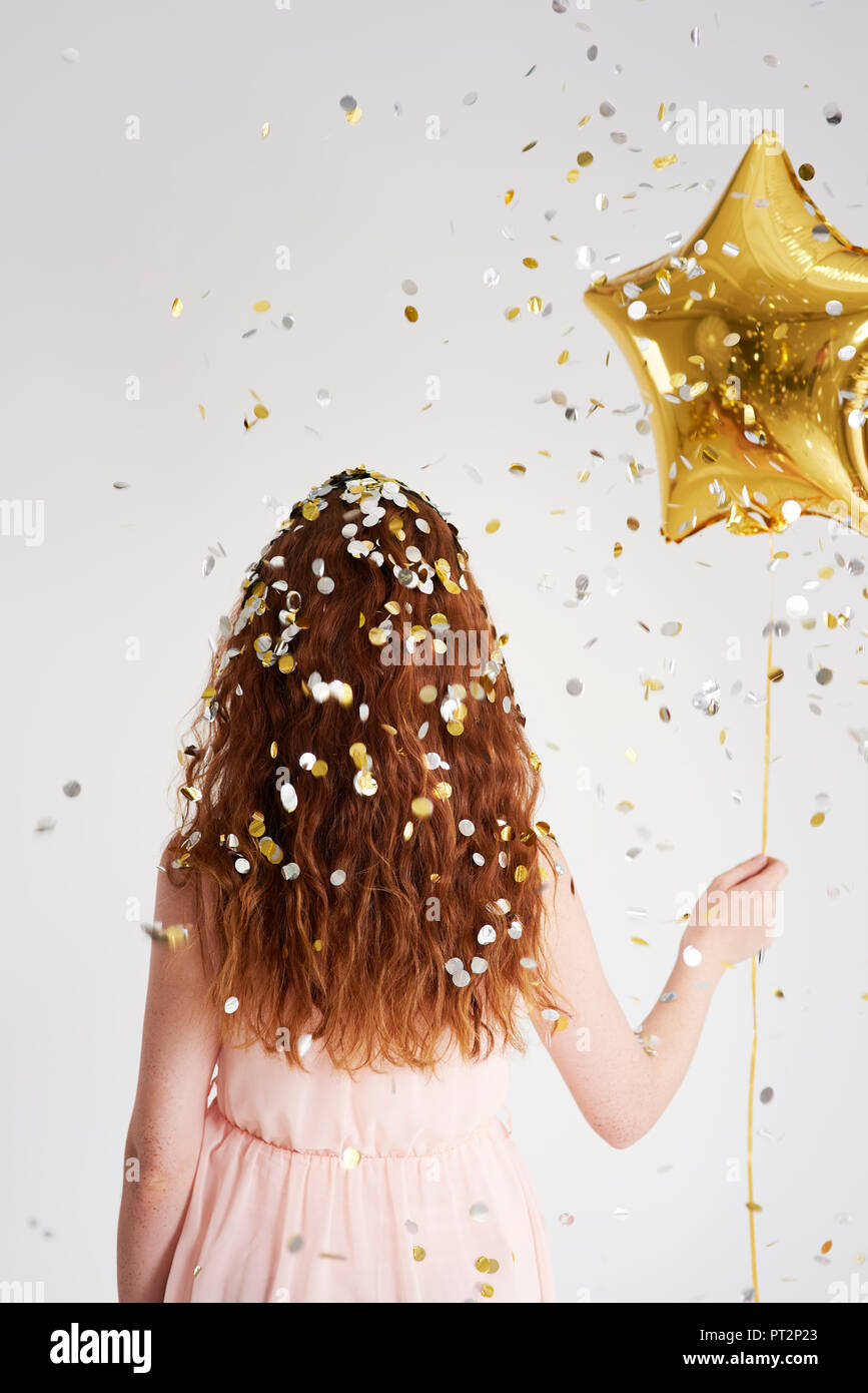 Vue arrière de jeune femme rousse avec ballon d'or en forme d'étoile sous pluie de confettis Banque D'Images