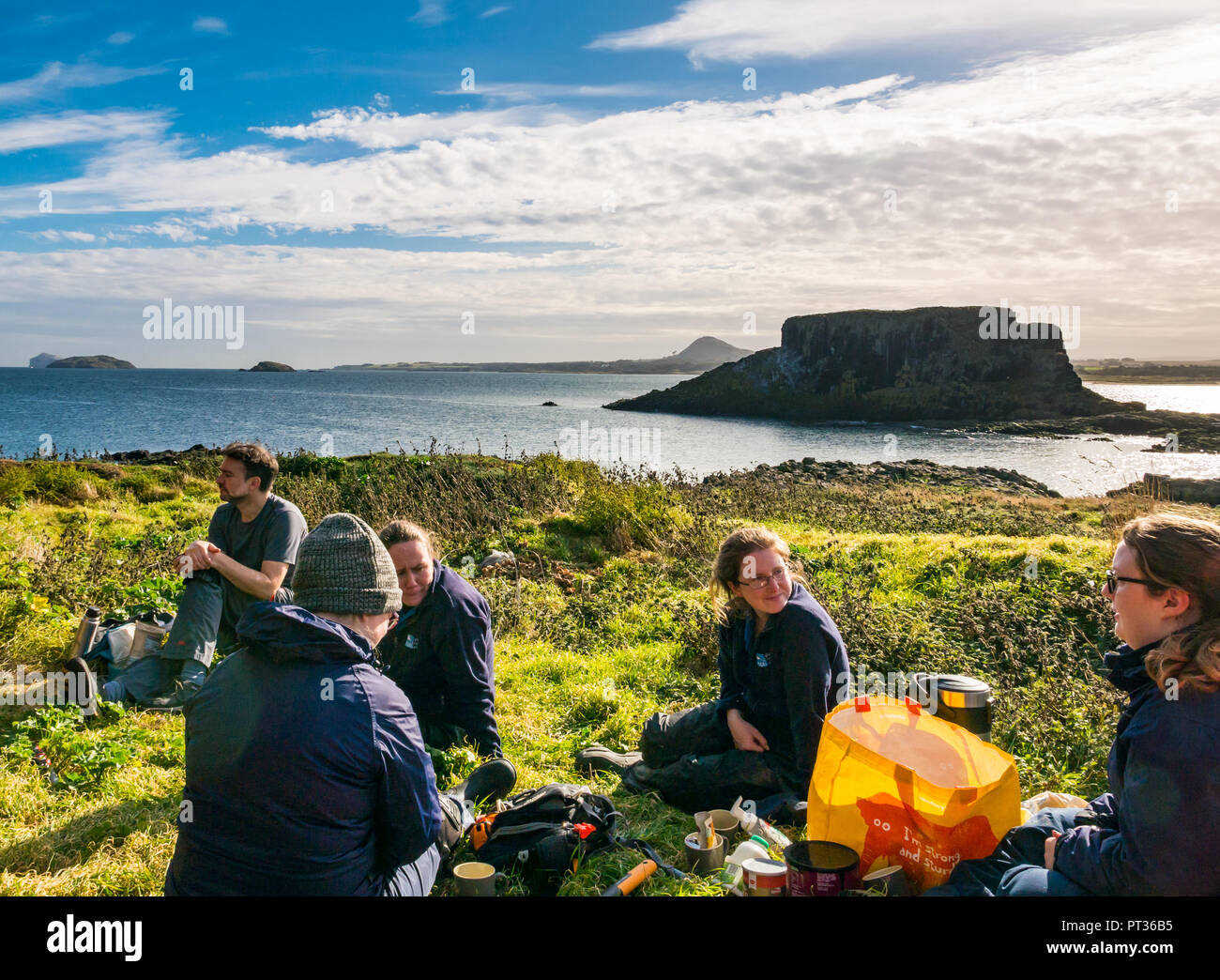 Groupe de travail RSPB pour effacer tree mallow prendre une pause sur l'île de Fidra, avec vue sur le Firth of Forth et de la côte d'East Lothian, Scotland, UK Banque D'Images