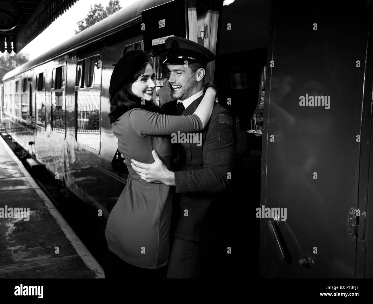 Vintage couple, bel homme en uniforme, embracing woman in dress et rire sur plate-forme comme train arrive en gare de chemin de fer Banque D'Images