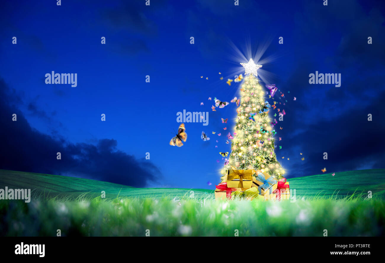 Décoration arbre de Noël brillant conceptuel sur paysage vert et de papillons volant au ciel nocturne clair Banque D'Images