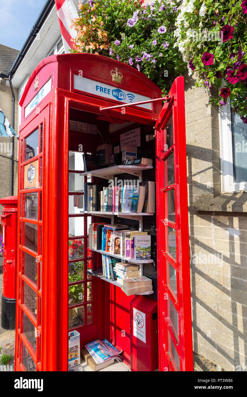Ancien BT téléphone rouge fort transformé en une mini-bibliothèque aide vous-même de second hand books, 22, de la rue principale de Beer, Devon, Angleterre Banque D'Images