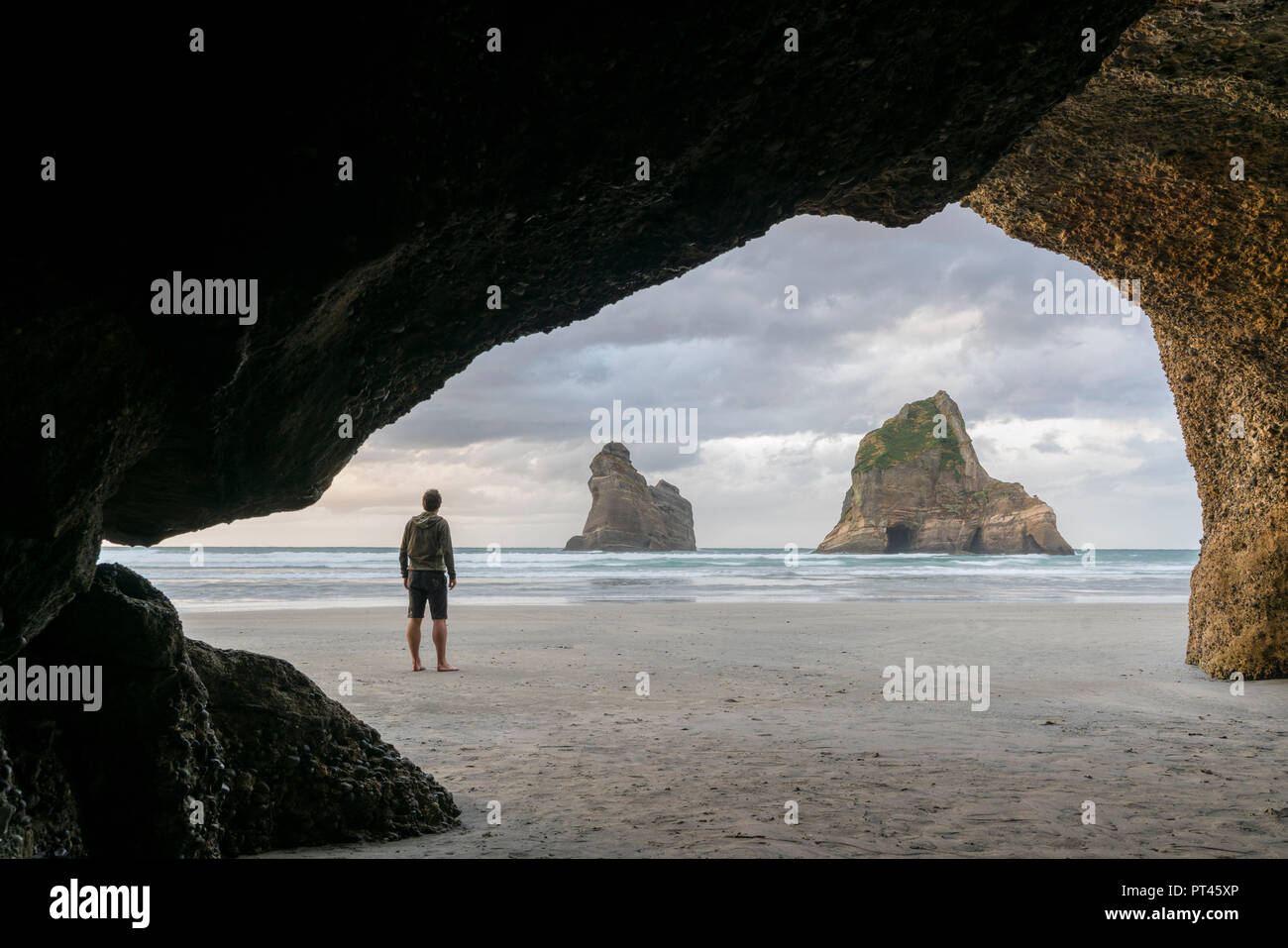 L'homme regardant deux des îles d'Archway, Wharariki beach, Puponga, district de Tasmanie, île du Sud, Nouvelle-Zélande, Banque D'Images