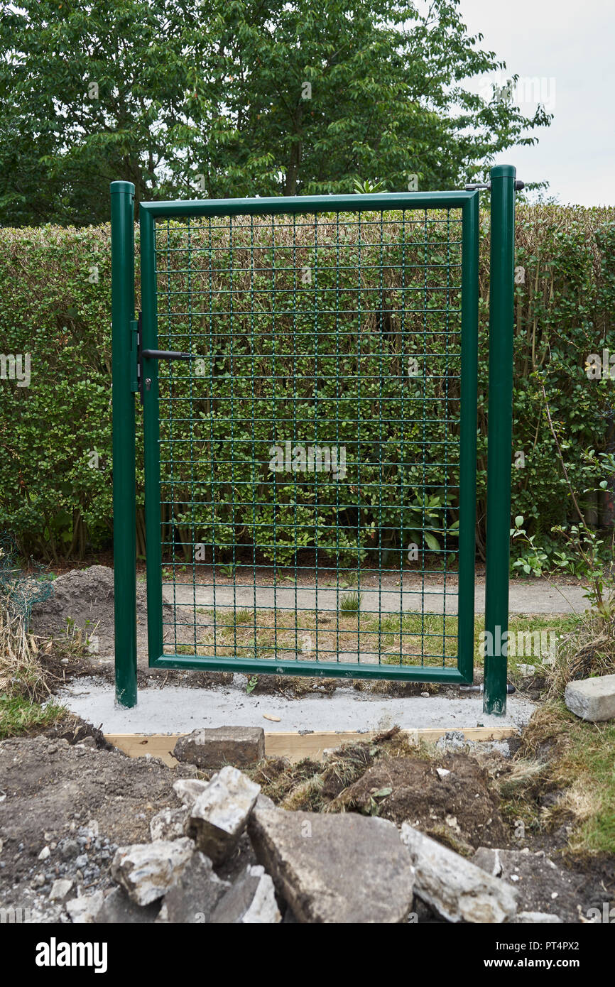 Construction jardin l'installation d'un nouveau métal vert porte d'entrée et de clôture autour du périmètre de la sûreté et de la sécurité dans l'foregroun avec terrassements Banque D'Images