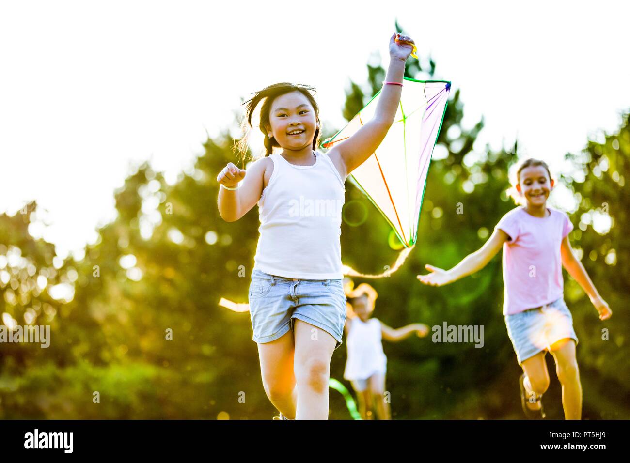 Fille courir avec kite et deux filles exécutant derrière elle dans le parc. Banque D'Images