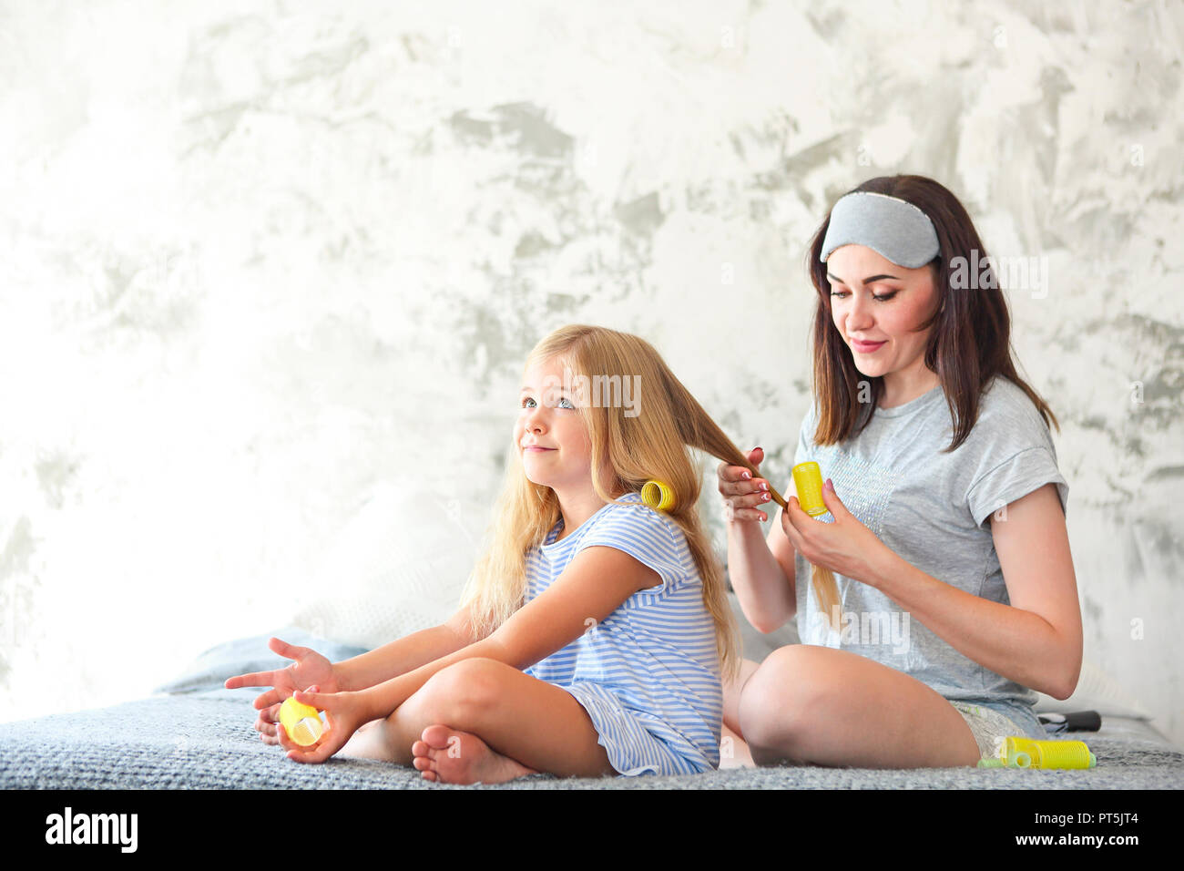 Jolie mère est le curling ses filles les cheveux. Femme et fille sont assis sur un lit Banque D'Images