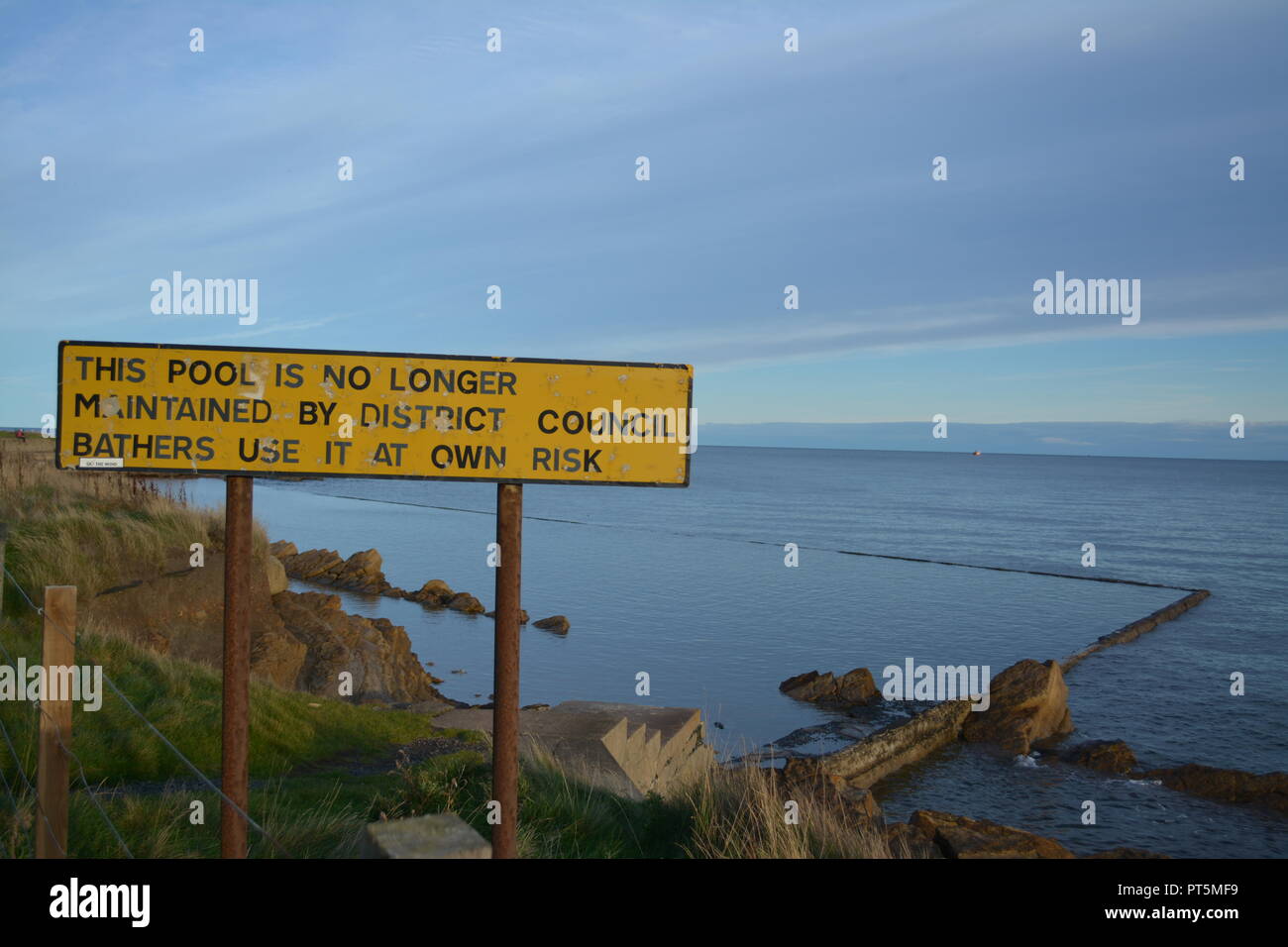Piscine extérieure dans la mer à St Monans Fife Scotland UK Royaume-Uni avec grand panneau jaune re les compressions des dépenses du Conseil de négligence des commodités locales Banque D'Images