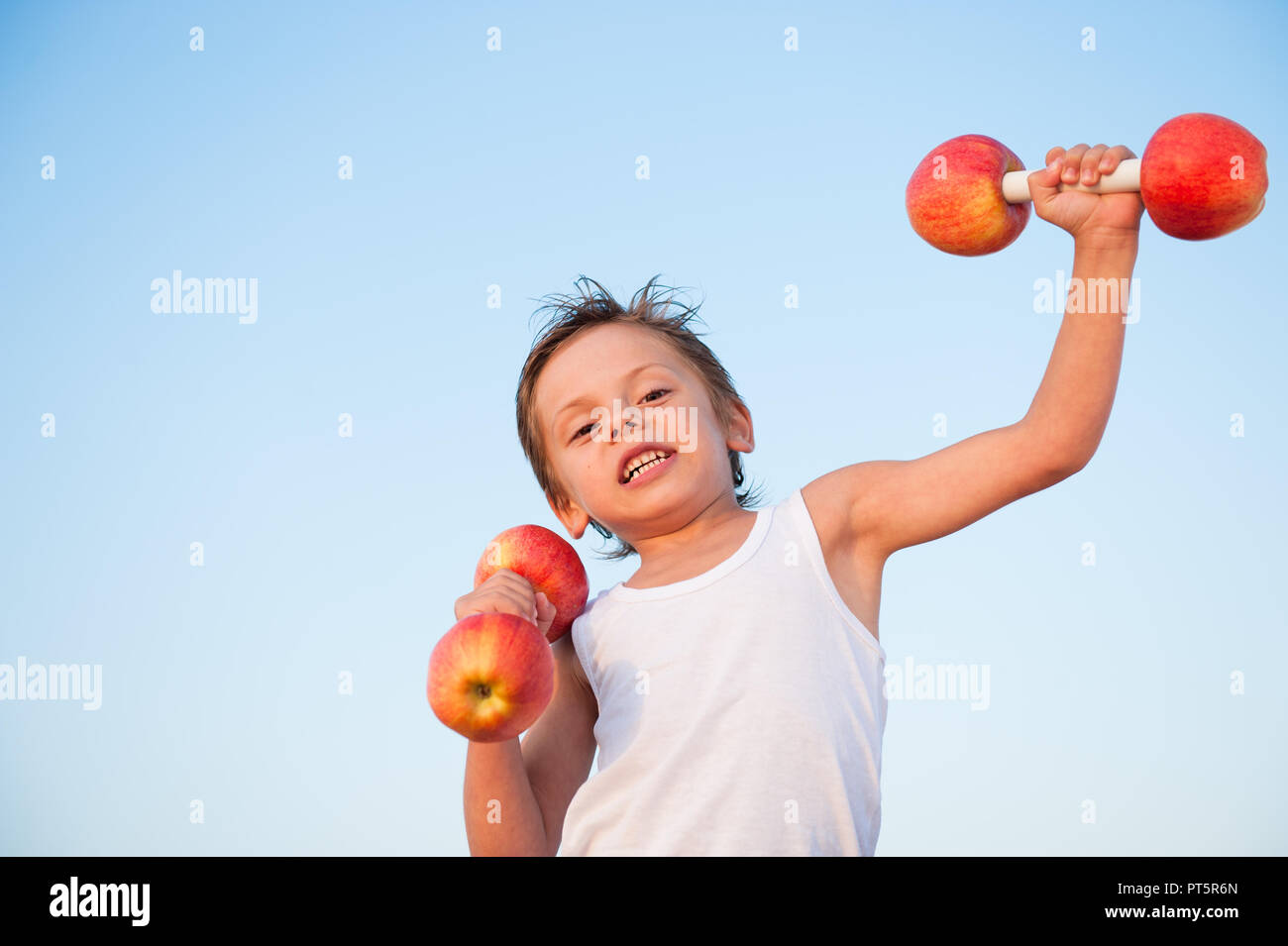 Mignon solide caucasian kid en chemise blanche haltères de levage fabriqués à partir de pommes fraîches Banque D'Images