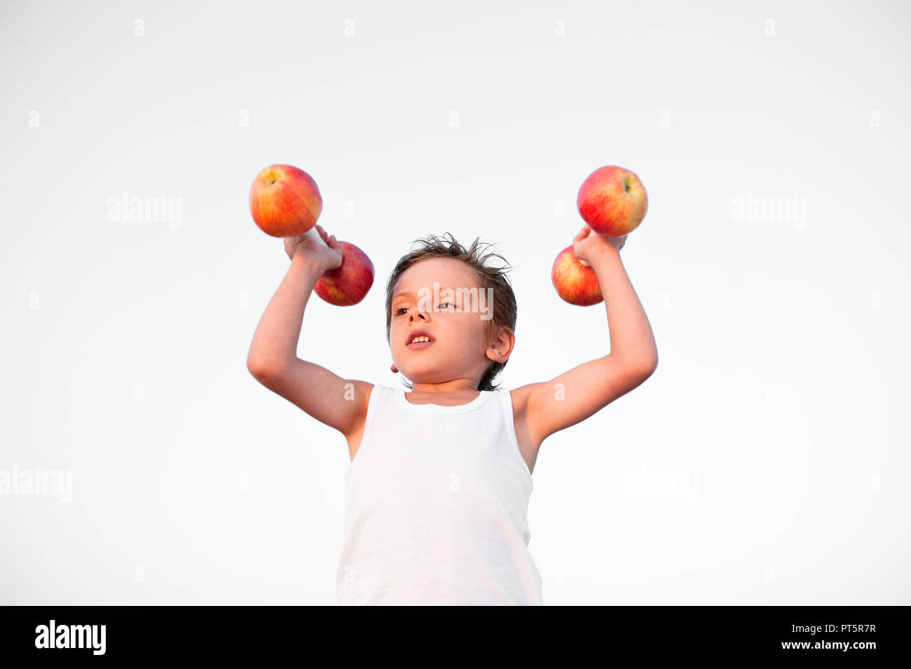 Mignon solide caucasian kid en chemise blanche haltères de levage fabriqués à partir de pommes fraîches Banque D'Images