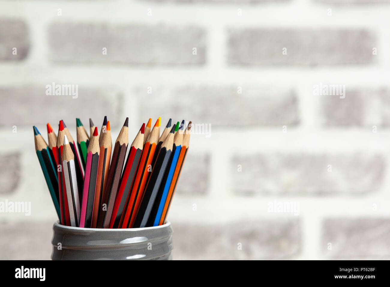 Ensemble de crayons de couleur stockées dans un pot en argile haut vis gris contre un mur de brique blured Banque D'Images