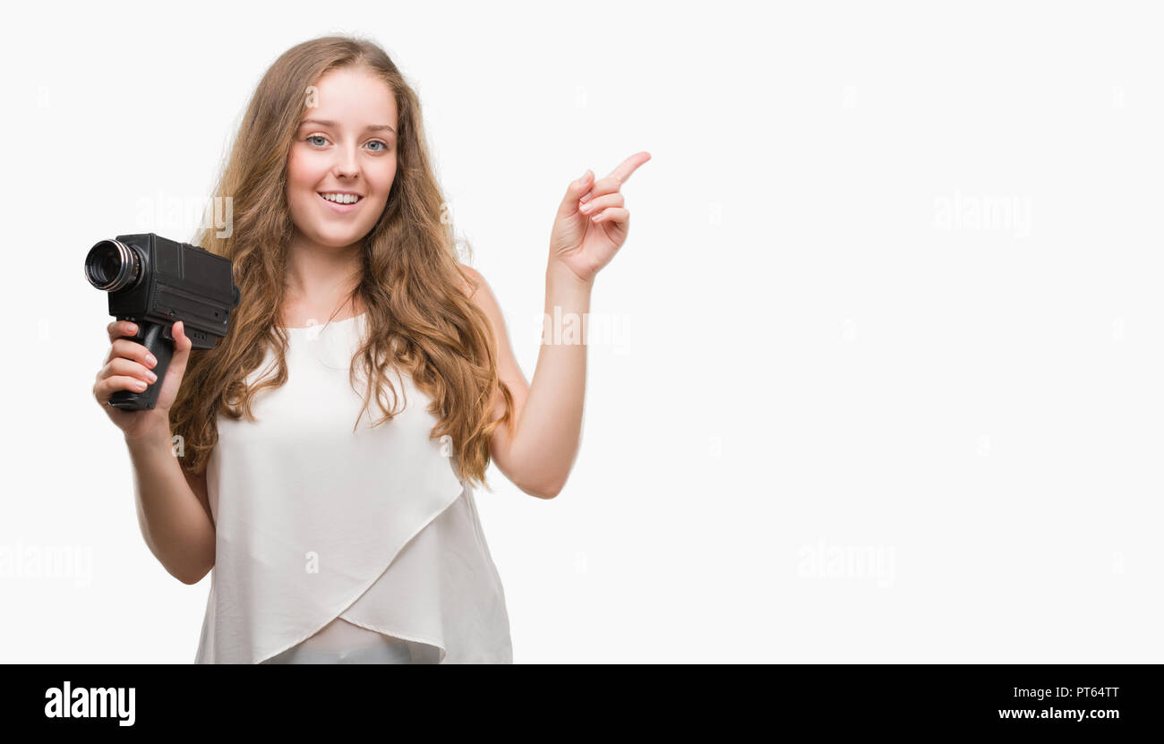 Jeune blond woman holding super 8 caméra vidéo très heureux pointant avec la main et le doigt sur le côté Banque D'Images