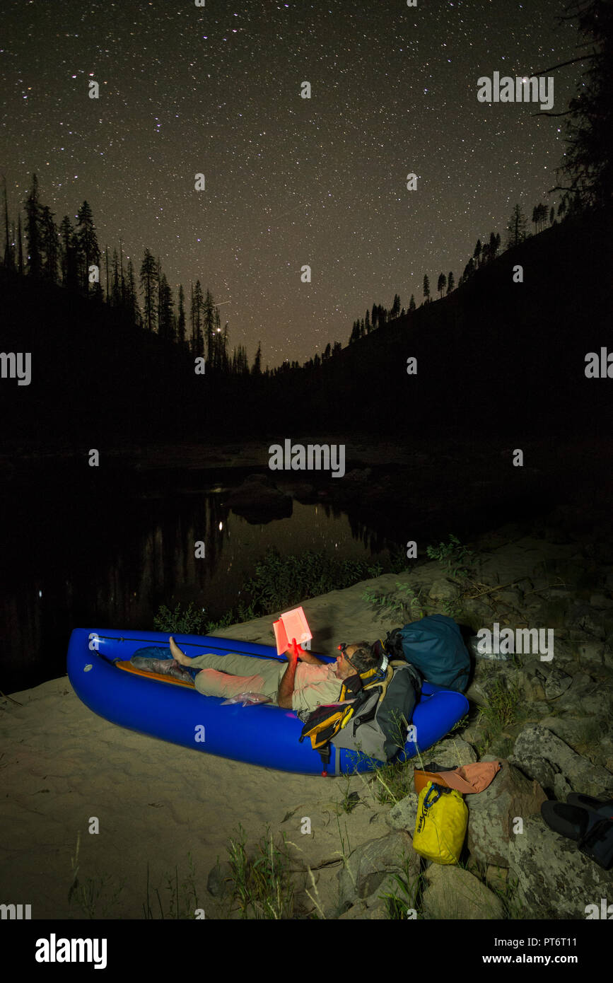 La lecture d'un livre la nuit portant dans un kayak gonflable dans un camping sur la rivière Selway de l'Idaho. Banque D'Images