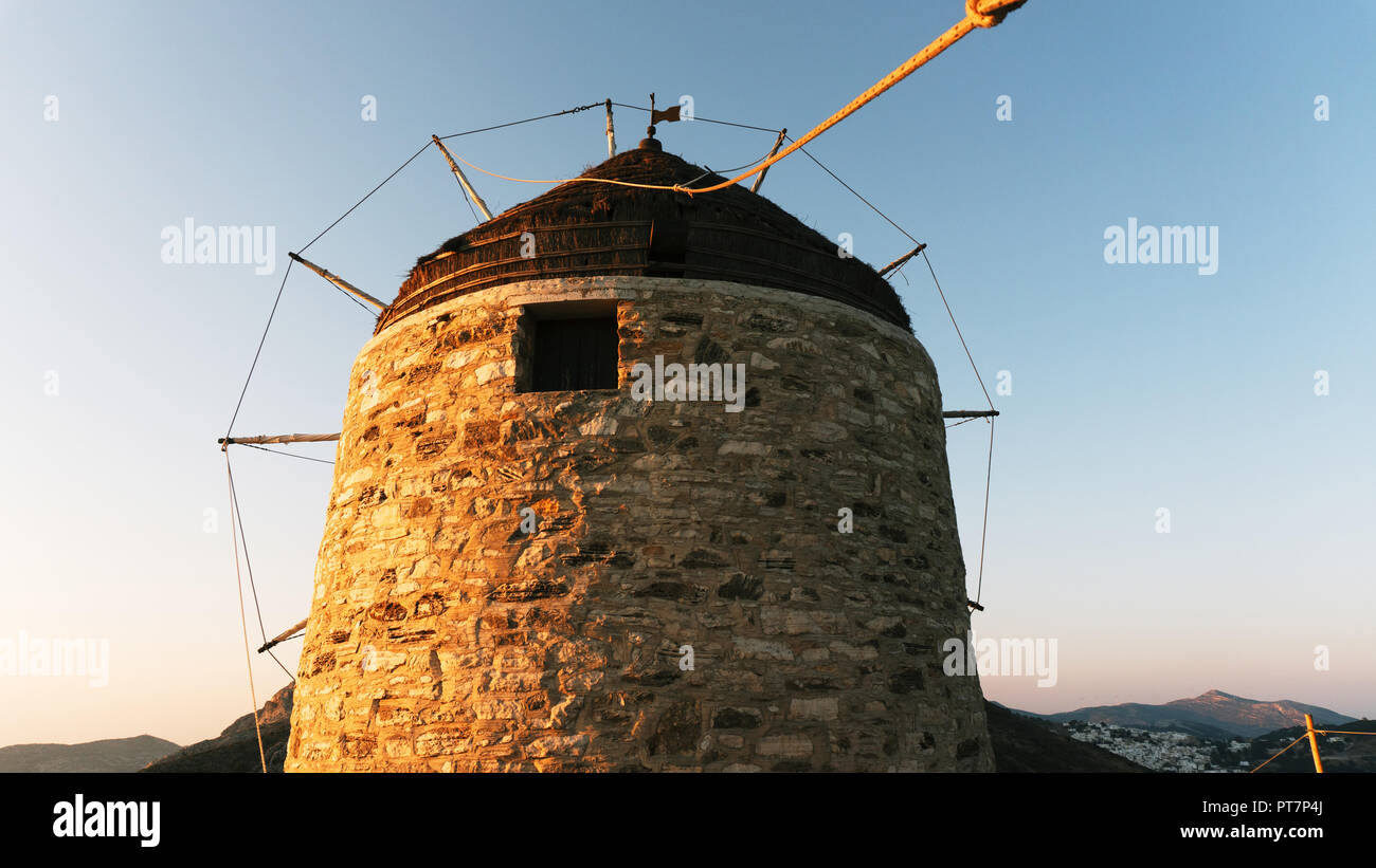 Un vieux moulin en pierre au sommet d'une montagne, dans le contexte d'une chaîne de montagnes et la vallée avec une petite ville aux maisons blanches sur une île grecque Banque D'Images