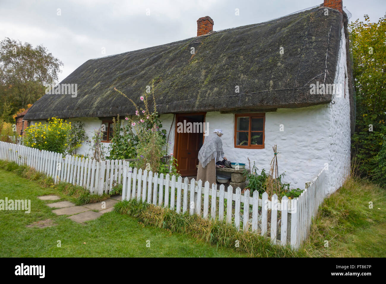 Cottage blanc fin du 18e siècle Cruck construction avec femme en robe en période jardin à Ryedale Folk Museum dans Hutton le Hole North Yorkshire Angleterre Banque D'Images