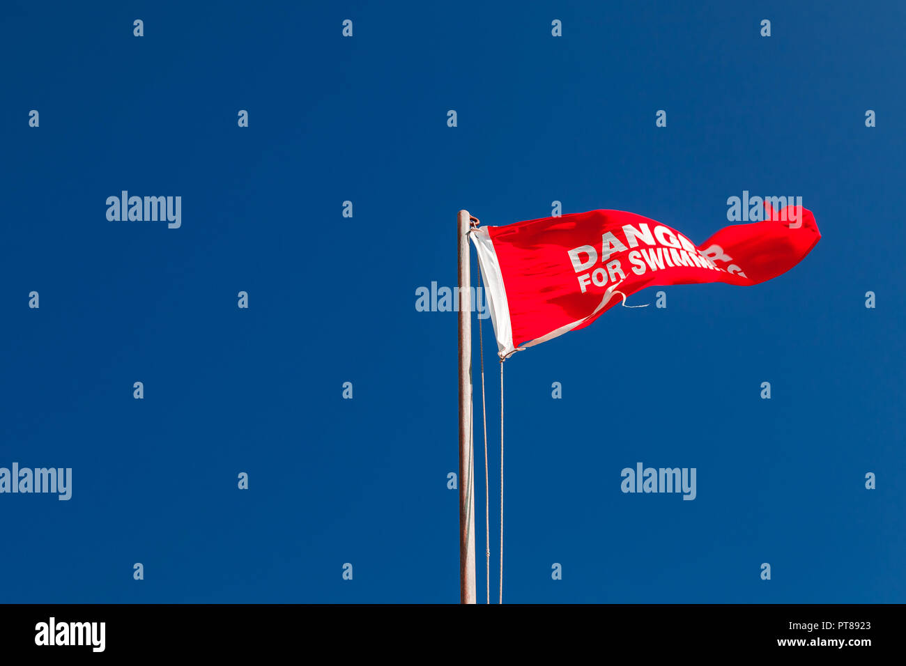 Danger pour la baignade. Triangle rouge drapeau sur une plage en agitant au-dessus de ciel bleu Banque D'Images