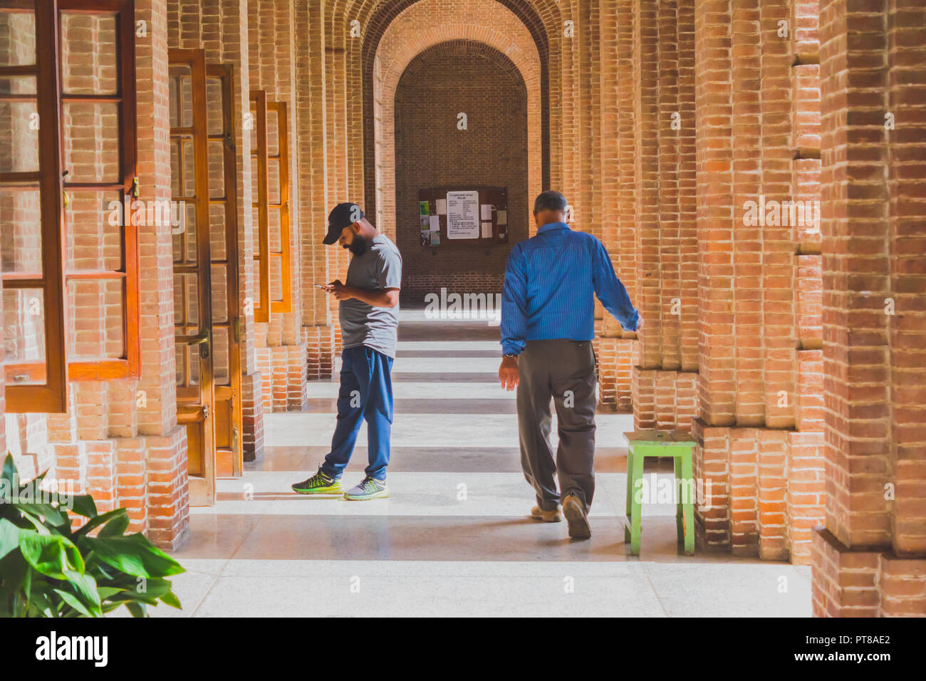 Une allée d'un bâtiment de l'architecture gréco-romaine avec un jeune homme barbu occupé avec le smartphone et un homme d'âge moyen en vous promenant le long de l'allée je Banque D'Images