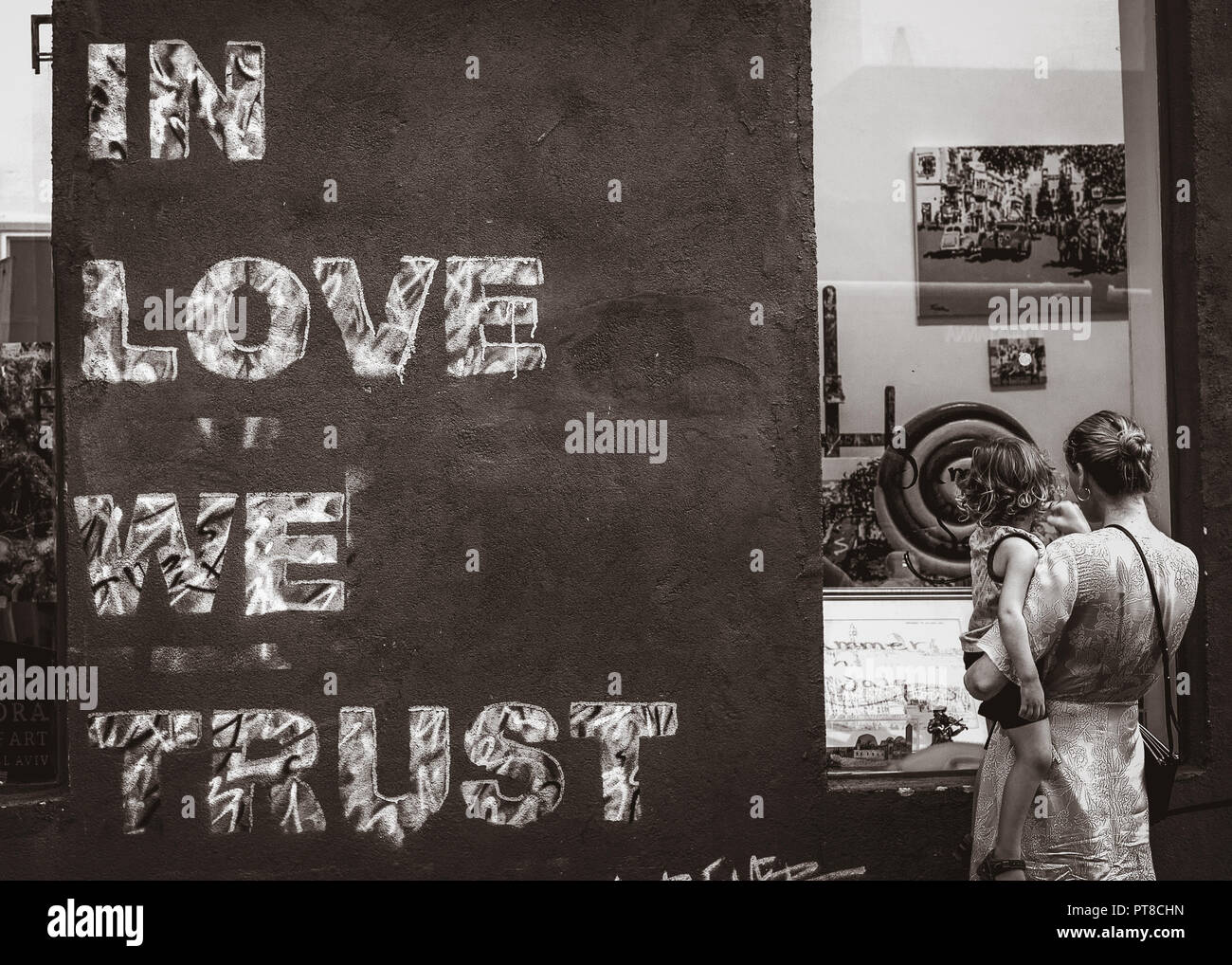 Mère tenant un enfant dans ses bras près d'un mur de graffiti dans l'amour nous faisons confiance au texte Neve Tzedek à Tel Aviv, Israël Banque D'Images