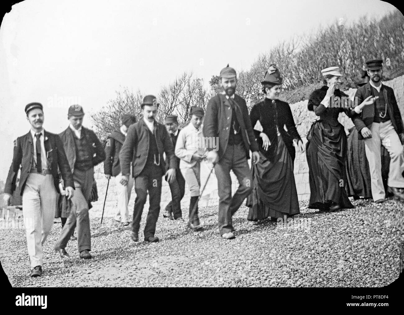 Photographie prise à la fin de l'époque victorienne agroup montrant des gens se promener le long d'une plage de galets quelque part en Angleterre. Typique de la mode montre la période. Banque D'Images
