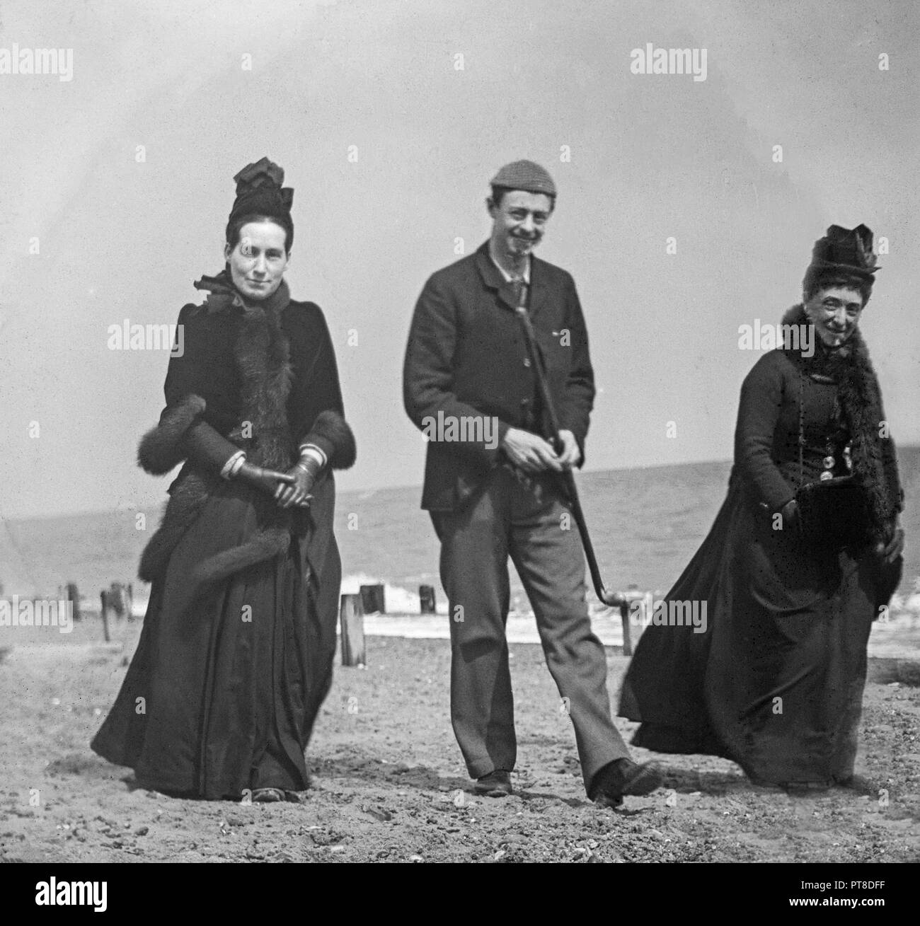 A la fin de photo d'un homme et deux femmes se promenant le long d'une plage en Angleterre. Montre de bons exemples de la mode de la période. Banque D'Images