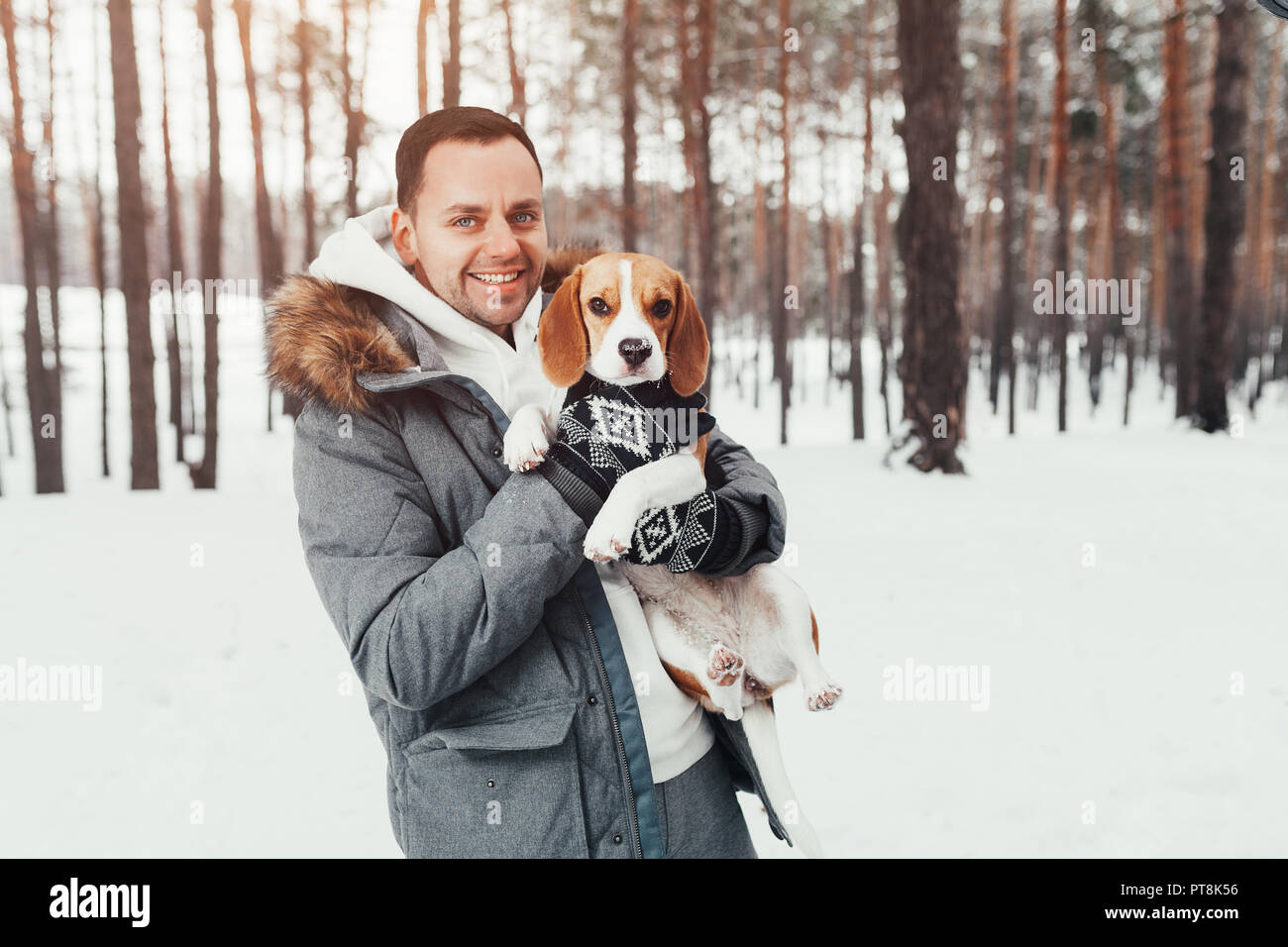 Un jeune homme habillé en hiver gris parc dans une forêt d'hiver neigeux est titulaire d'un chien nommé Beagle. Concept à propos de loisirs d'hiver et de l'amour pour les animaux Banque D'Images