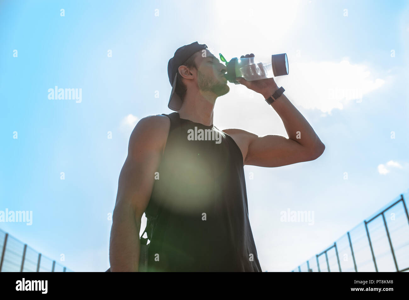 Taille portrait of handsome young sportsman l'eau potable après entraînement à l'extérieur debout contre le ciel, lens flare Banque D'Images