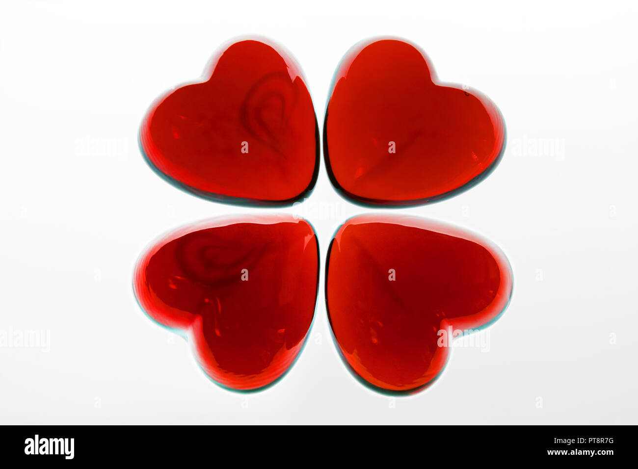 Trèfle à Quatre Feuilles faites avec des coeurs en verre rouge sur une surface transparente. Banque D'Images
