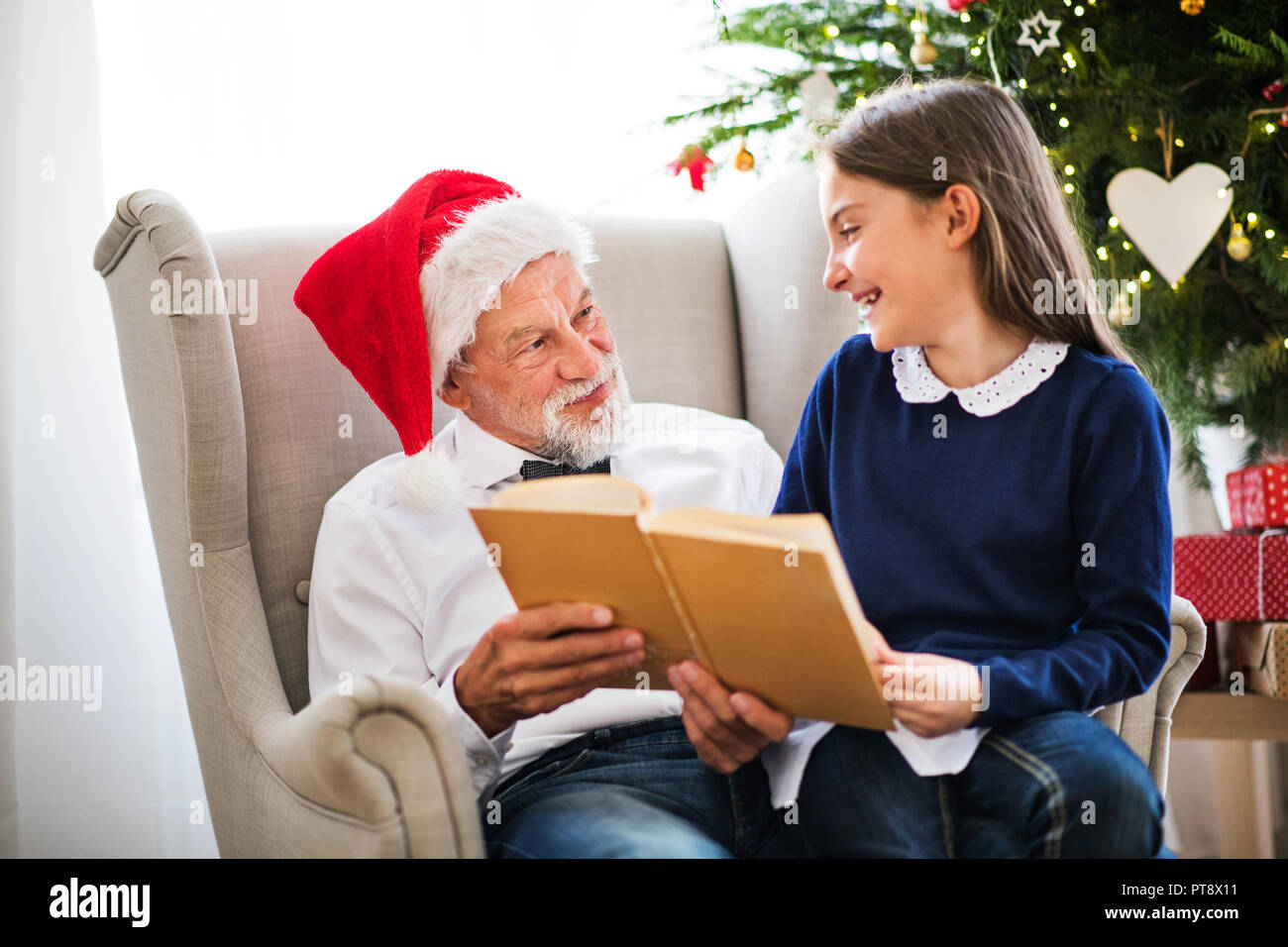 Une petite fille et de son grand-père avec Santa hat de lire un livre à l'époque de Noël. Banque D'Images