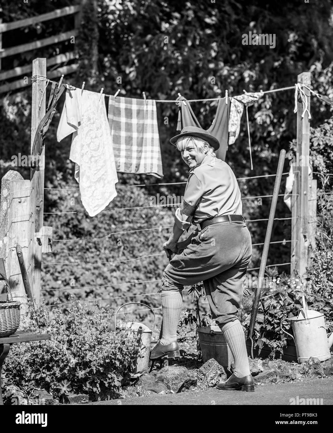 Vue arrière en noir et blanc de la femme souriante dehors au soleil, en costume, regardant en arrière au-dessus de l'épaule creusant Dig pour le jardin de la Victoire, l'événement de la seconde Guerre mondiale des années 1940 au Royaume-Uni. Banque D'Images