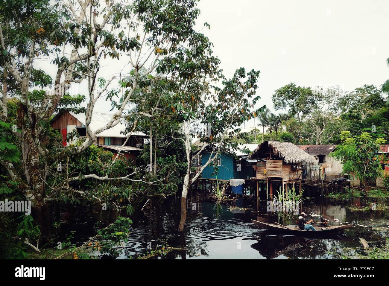 Des maisons sur pilotis sur le fleuve Amazone en Colombie avec un homme sur une pirogue Banque D'Images