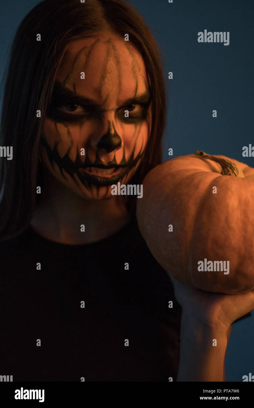 Une fille dans un masque de l'homme mort avec une citrouille sur un fond sombre. Halloween Banque D'Images