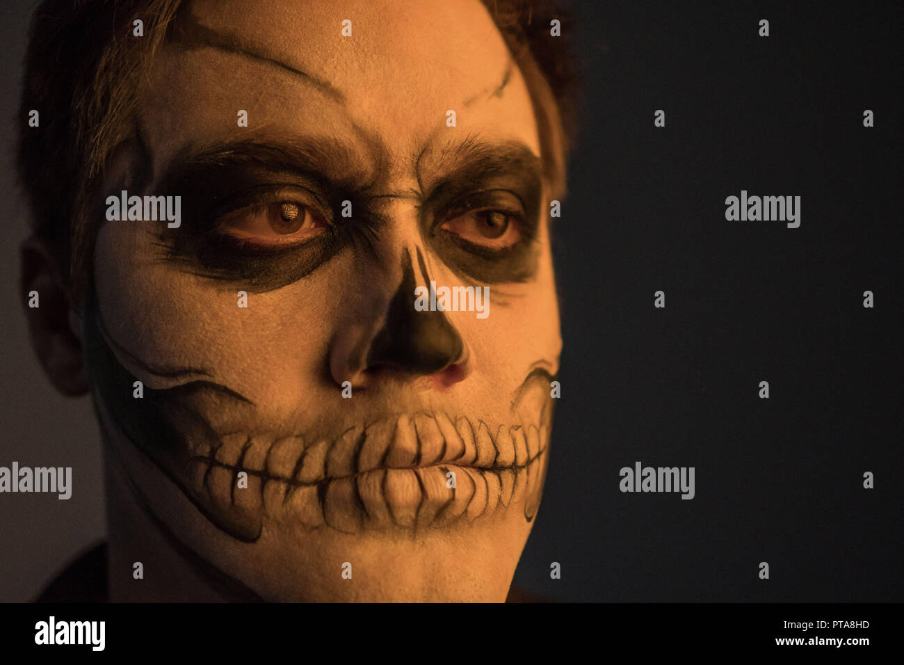 Portrait d'un jeune homme avec un crâne de maquillage pour Halloween sur fond noir Banque D'Images