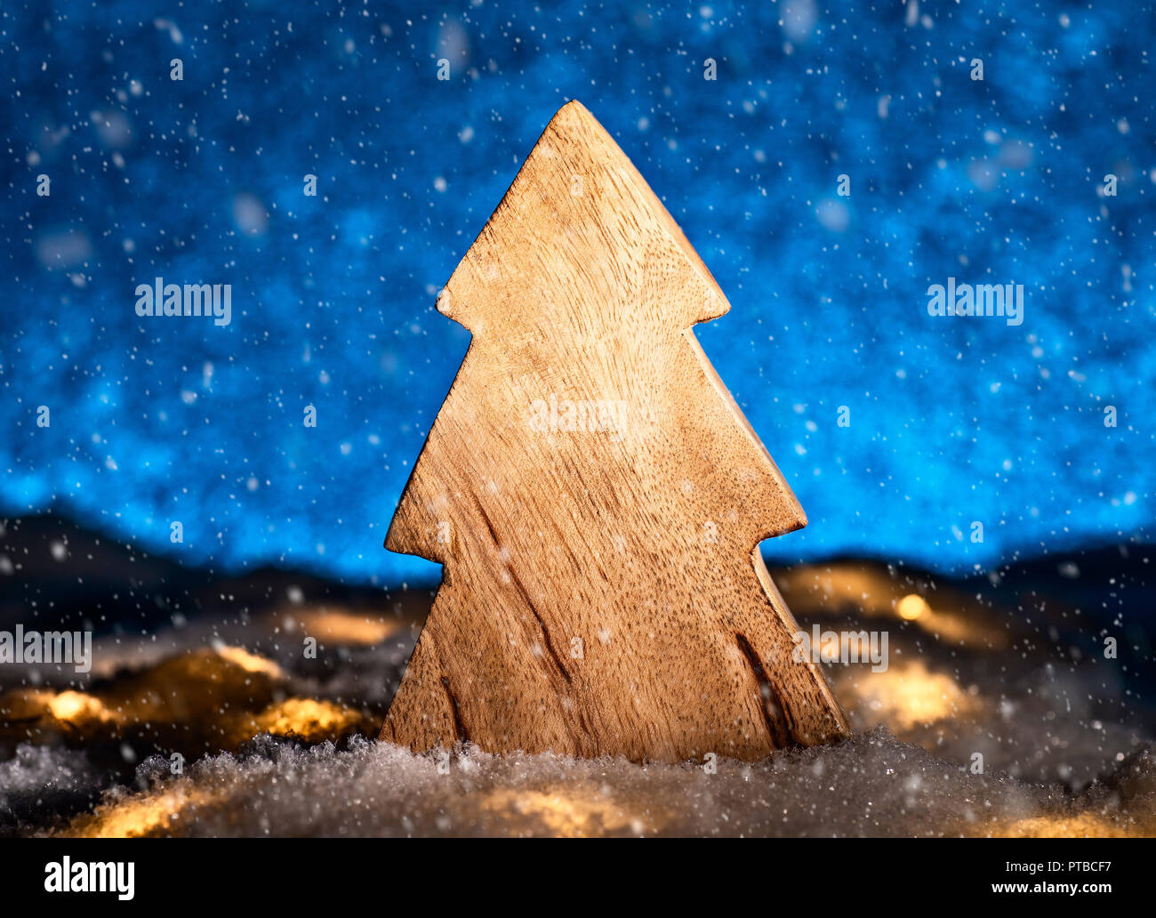 Arbre de Noël en bois avec la neige en face d'un fond bleu Banque D'Images