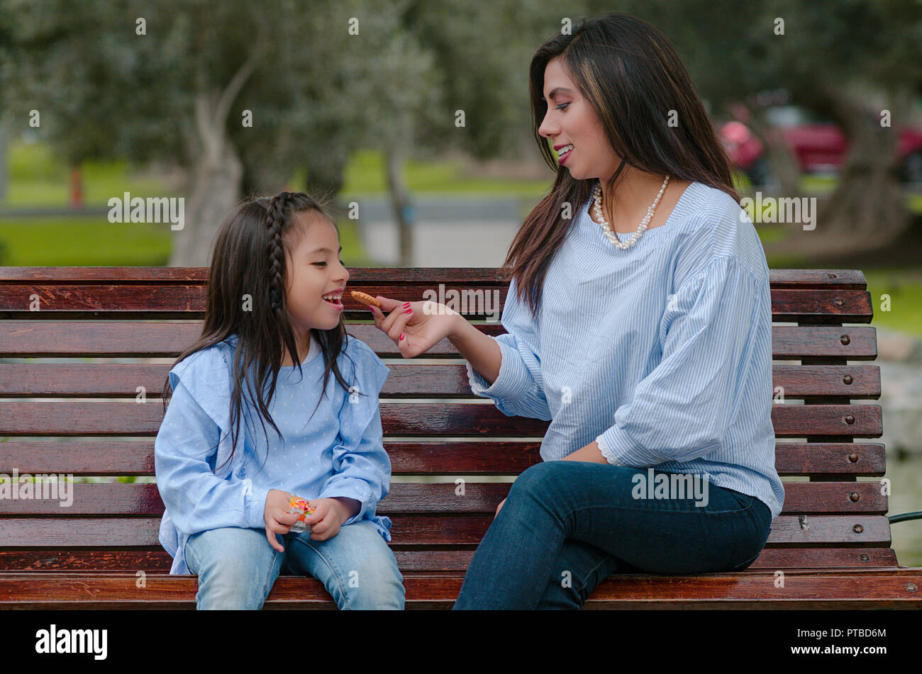 Mère et sa petite fille assise sur un banc de manger un cookie dans le parc Banque D'Images