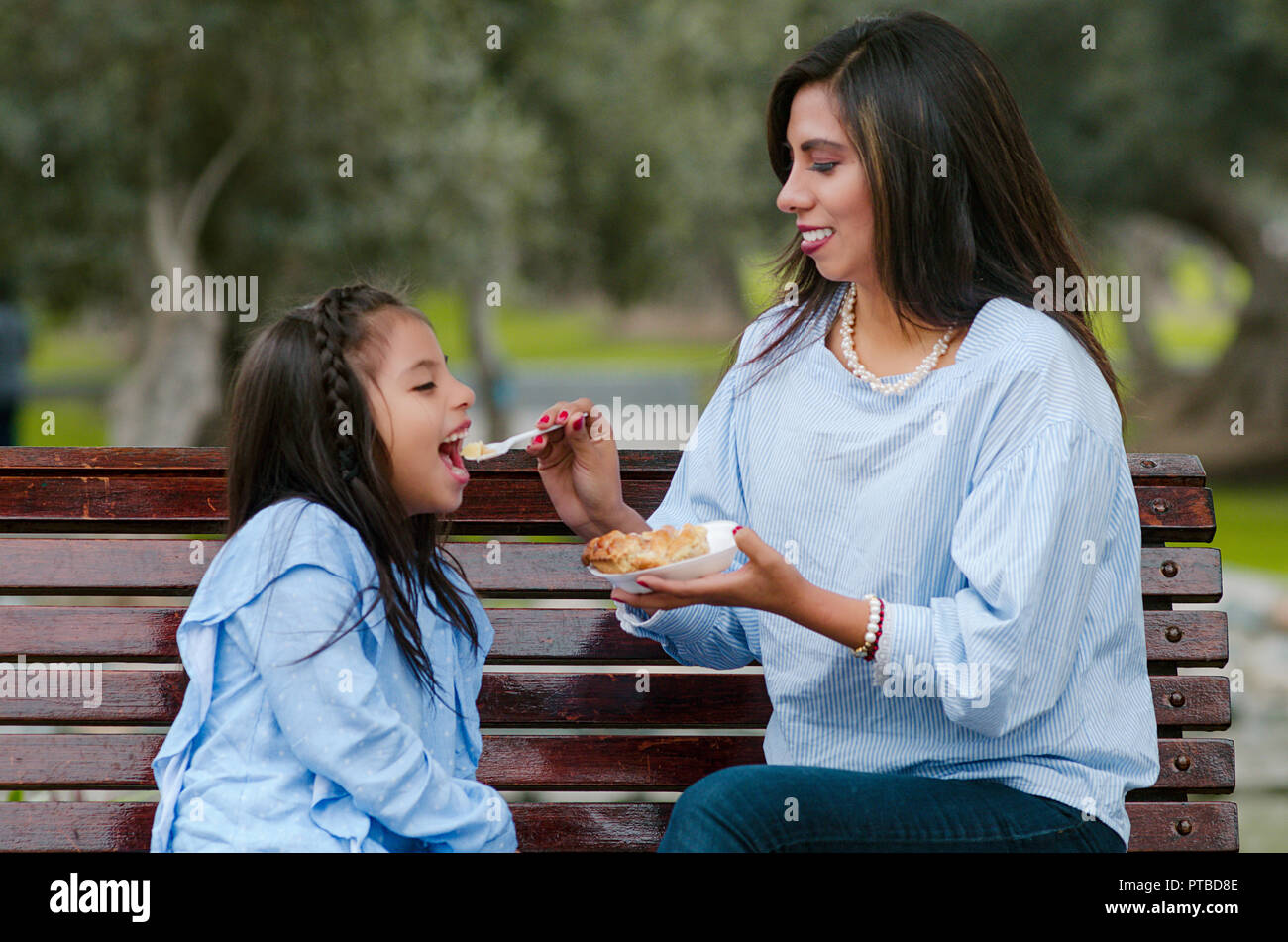 Mère et sa petite fille assise sur un banc dans le parc de manger un morceau de gâteau Banque D'Images