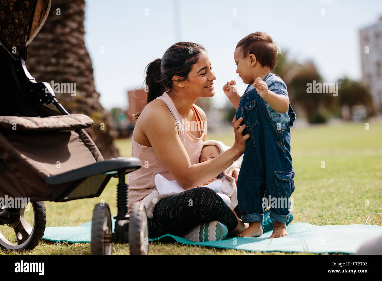Jeune mère assise sur un tapis de yoga au parc avec ses deux enfants dans la matinée. Woman relaxing in park avec les enfants après sa matinée de marche. Banque D'Images
