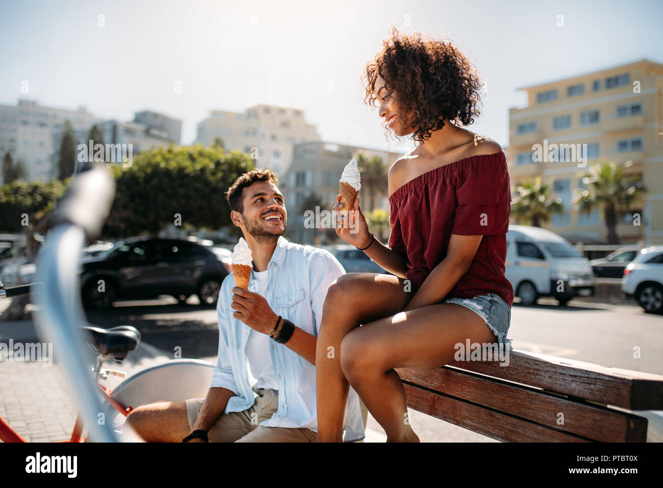 Couple assis sur un banc dans l'alimentation de rue à la crème glacée de cône à l'autre. Jeune homme et femme s'amusant se déplacer dans la ville de manger Banque D'Images