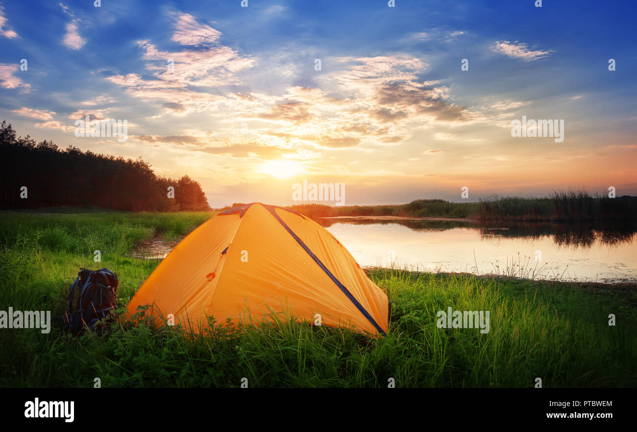 Par l'orange tente lac. Tente d'Orange se situe sur les rives de l'herbe verte au coucher du soleil. Le concept de la vie privée et les voyages. Banque D'Images