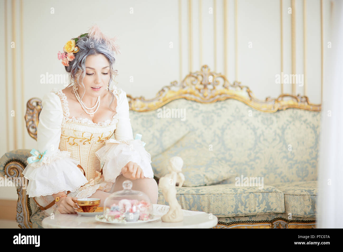Belle femme grayhead en robe Rococo posant devant fond rose en buvant du thé. halloween Banque D'Images