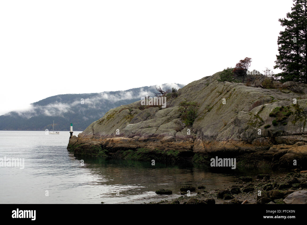 La côte rocheuse de Whytecliff Park, dans l'ouest de Vancouver, BC, Canada, sur un jour nuageux et pluvieux, montrant la mer et un voilier dans l'arrière-plan Banque D'Images