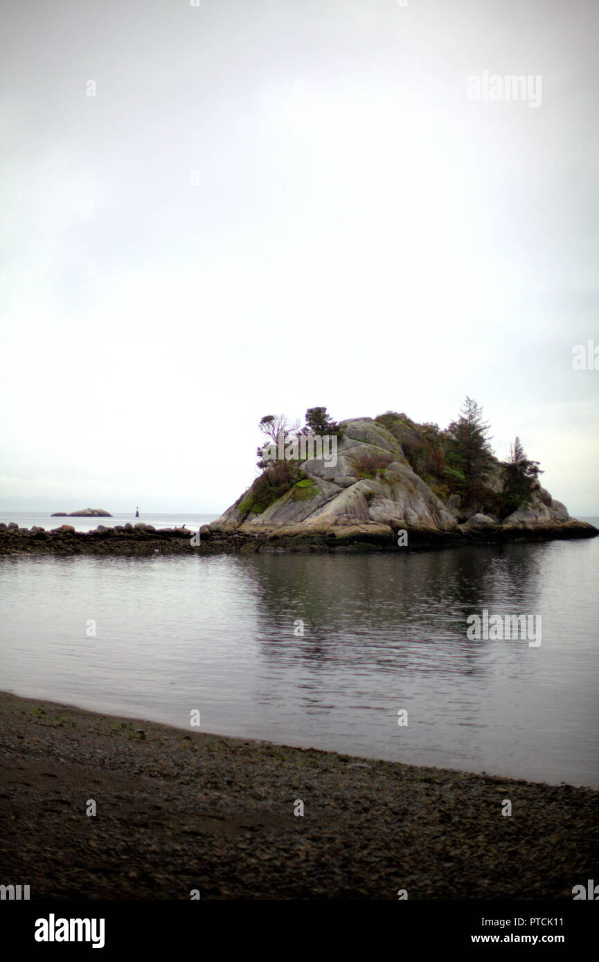 L'islet Whyte à Horseshoe Bay, BC, Canada, sur un jour de pluie de l'automne, montrant le ciel blanc, la mer calme et l'obscurité rocky shore Banque D'Images