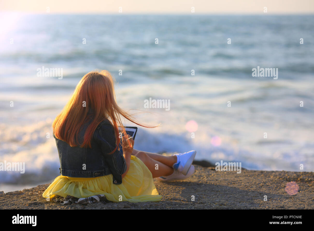 Red hair girl est artiste, c'est dessiner à l'extérieur. Elle est assise sur le quai de la mer en soirée et le dessin dans un carnet Banque D'Images