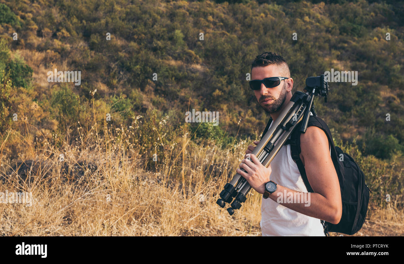 Le jeune photographe avec une barbe, sac à dos sur son dos et le trépied sur son épaule sur la montagne Banque D'Images