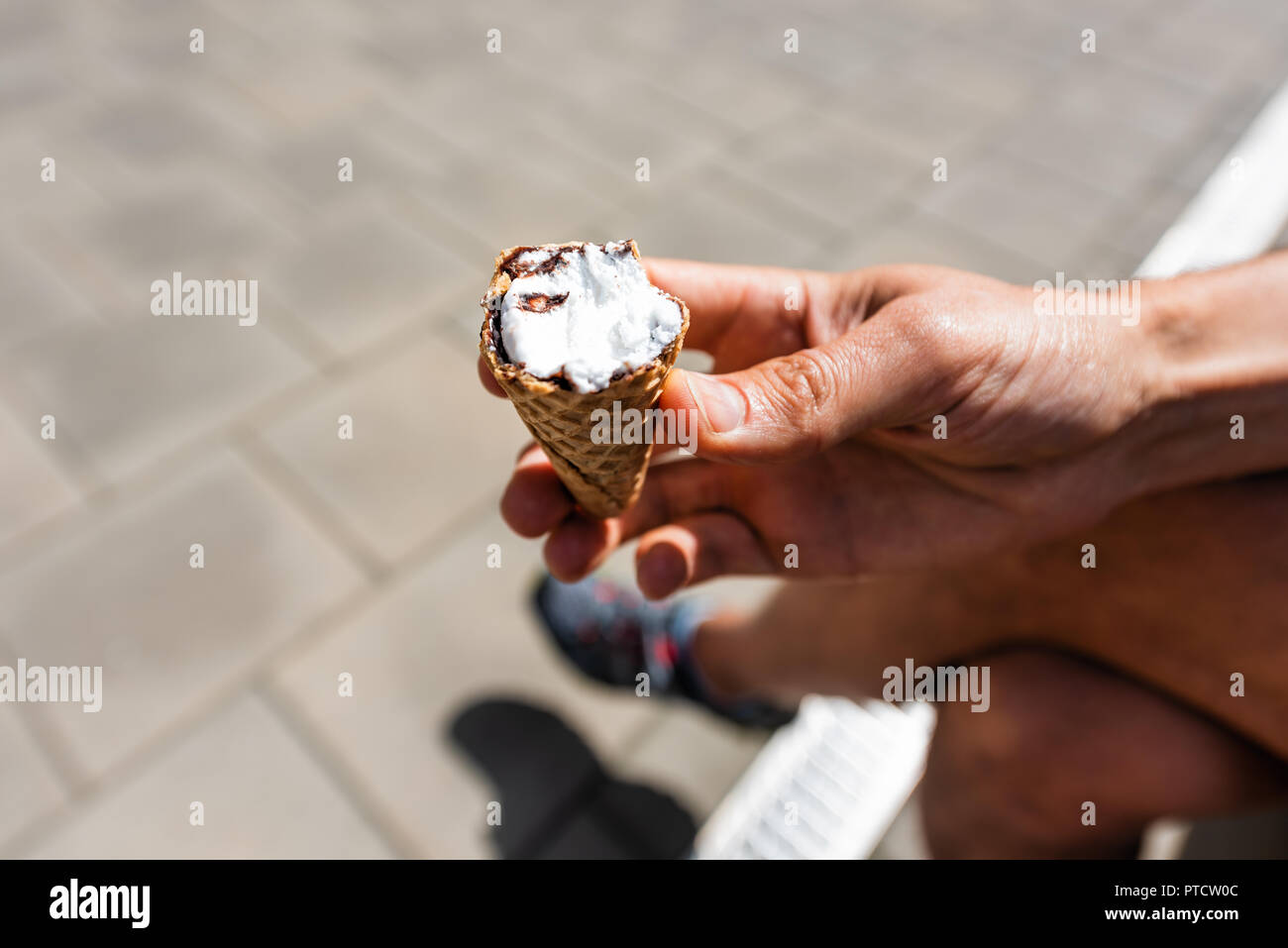 Homme tenant un livre blanc à moitié mangé de la glace à la vanille gelato italien cône sur la rue en ville, ville au cours de l'été chaud et ensoleillé jour Banque D'Images