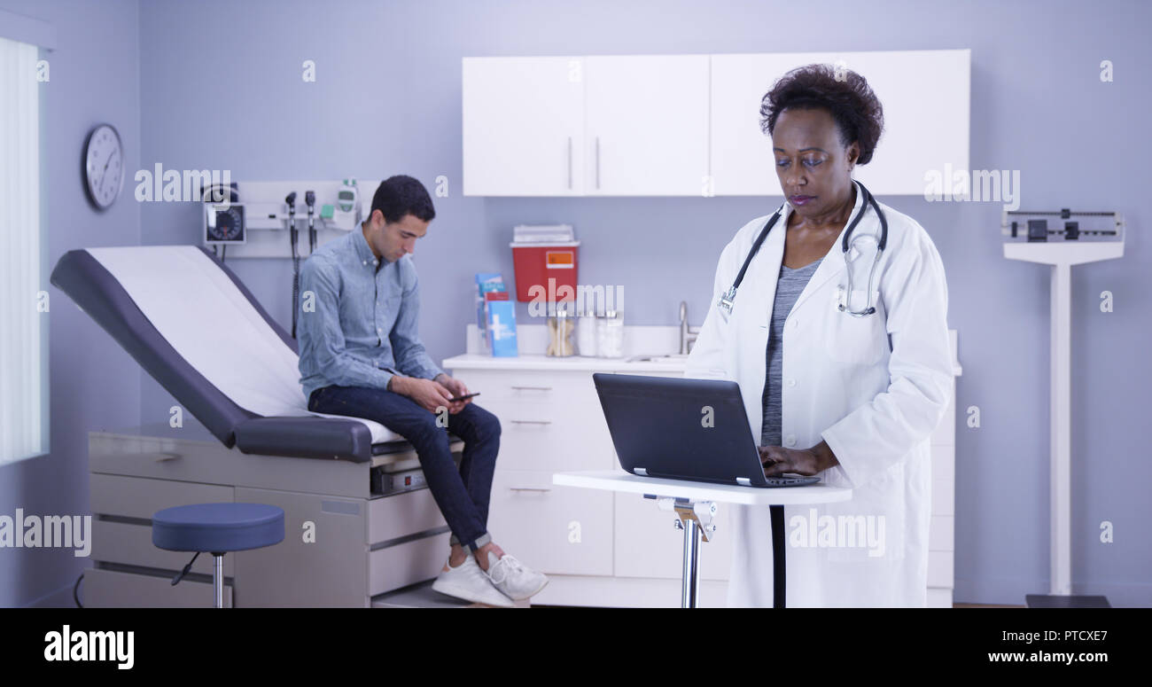 Les cadres supérieurs de prendre des notes de médecin noir seul patient latino sur l'ordinateur portable Banque D'Images Les cadres supérieurs de prendre des notes de médecin noir seul patient latino sur l'ordinateur portable Banque D'Images