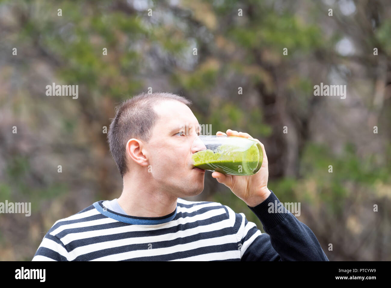 Jeune homme debout à l'extérieur, en plein air, la détention, la consommation d'alcool et de smoothie vert verre fabriqué à partir de légumes verts, Banque D'Images