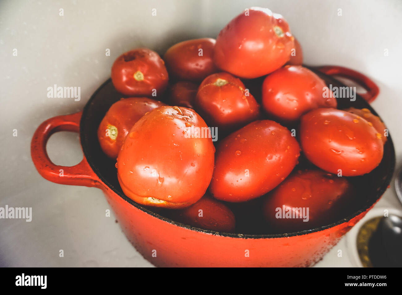 Close up of les tomates Roma couvert de gouttelettes d'eau dans le Creuset casserole rouge en blanc dans l'évier de cuisine gastronomique Banque D'Images