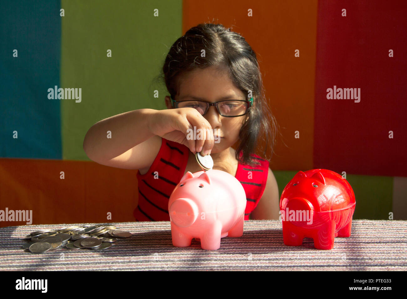 Petite fille essayant de mettre des pièces dans sa tirelire, Pune, Inde Banque D'Images