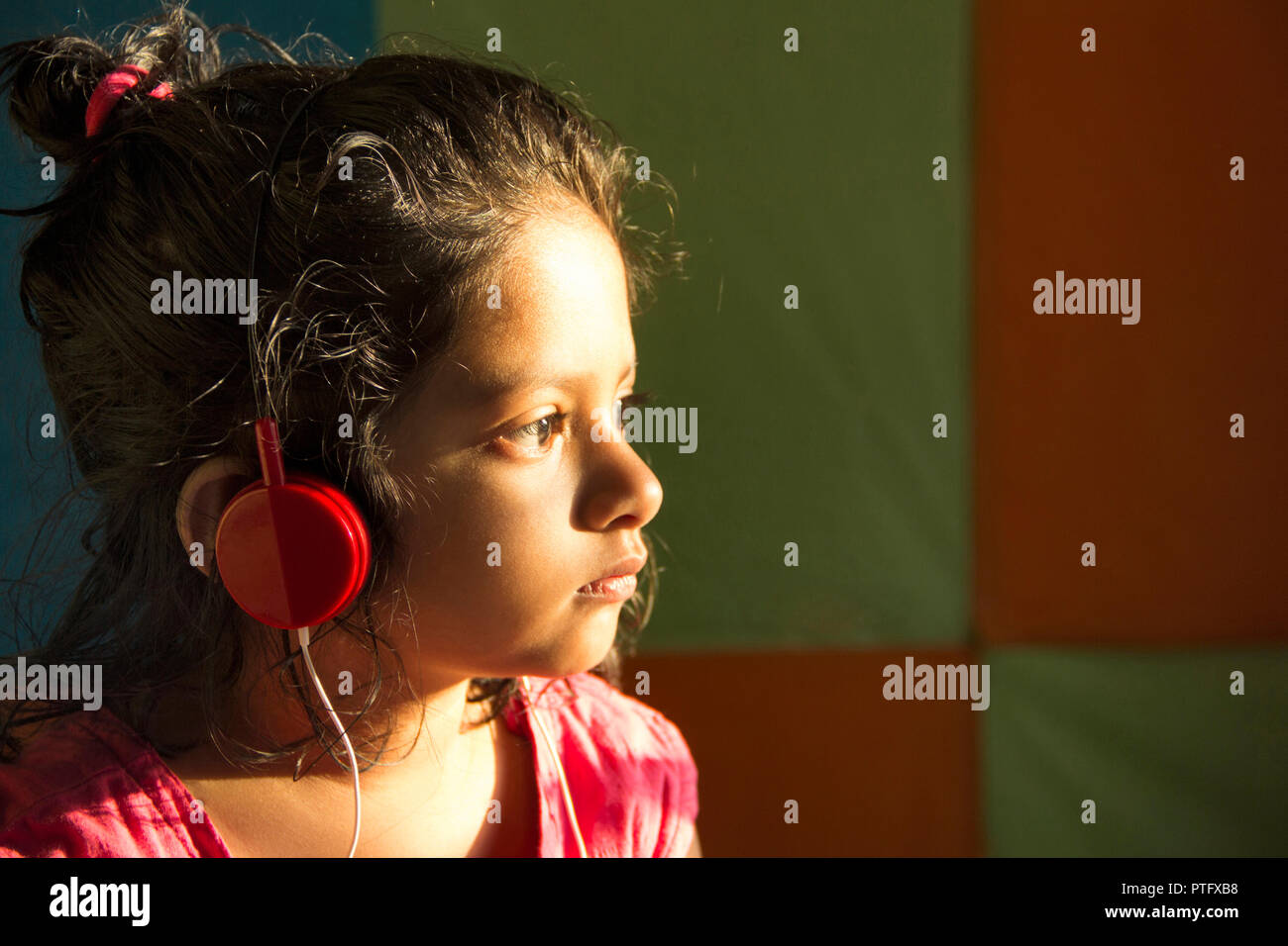 Close-up of little girl écoutez de la musique avec des écouteurs de couleur rouge dans la lumière du soleil, Pune, Inde Banque D'Images