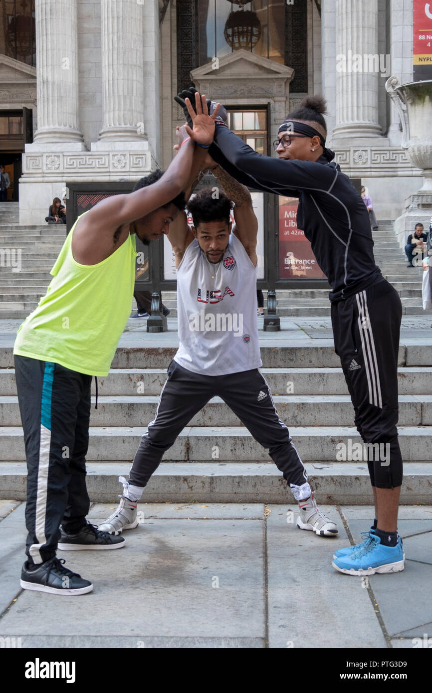 Les artistes de rue. Une équipe de breakdance acrobatique huddle buskers en face de la succursale principale de la Bibliothèque publique de New York sur la Cinquième Avenue. dans Manhattan. Banque D'Images