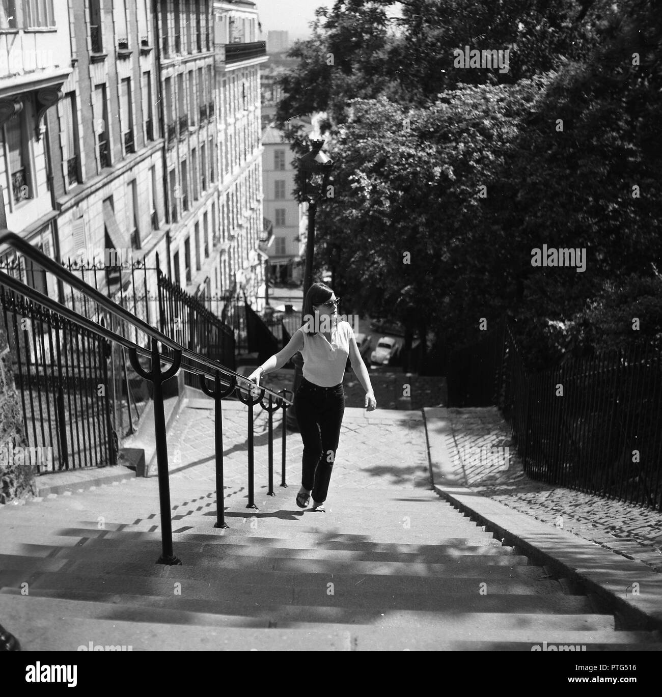 Années 1960, historiques, femme tenant le métal central garde-corps comme elle marche d'un escalier raide, la rue Foyatier à Montmartre, Paris, France. En haut de l'escalier sont les principales attractions de la région, y compris la Basilique du Sacré-Coeur. Banque D'Images