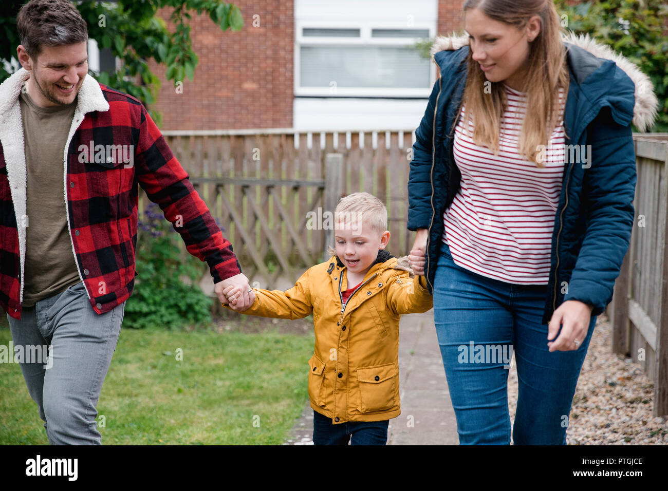 Little Boy holding hands ses parents comme ils marchent le long du chemin de jardin de revenir à la Chambre. Ils sont sourire et rire sur le chemin du retour. Banque D'Images